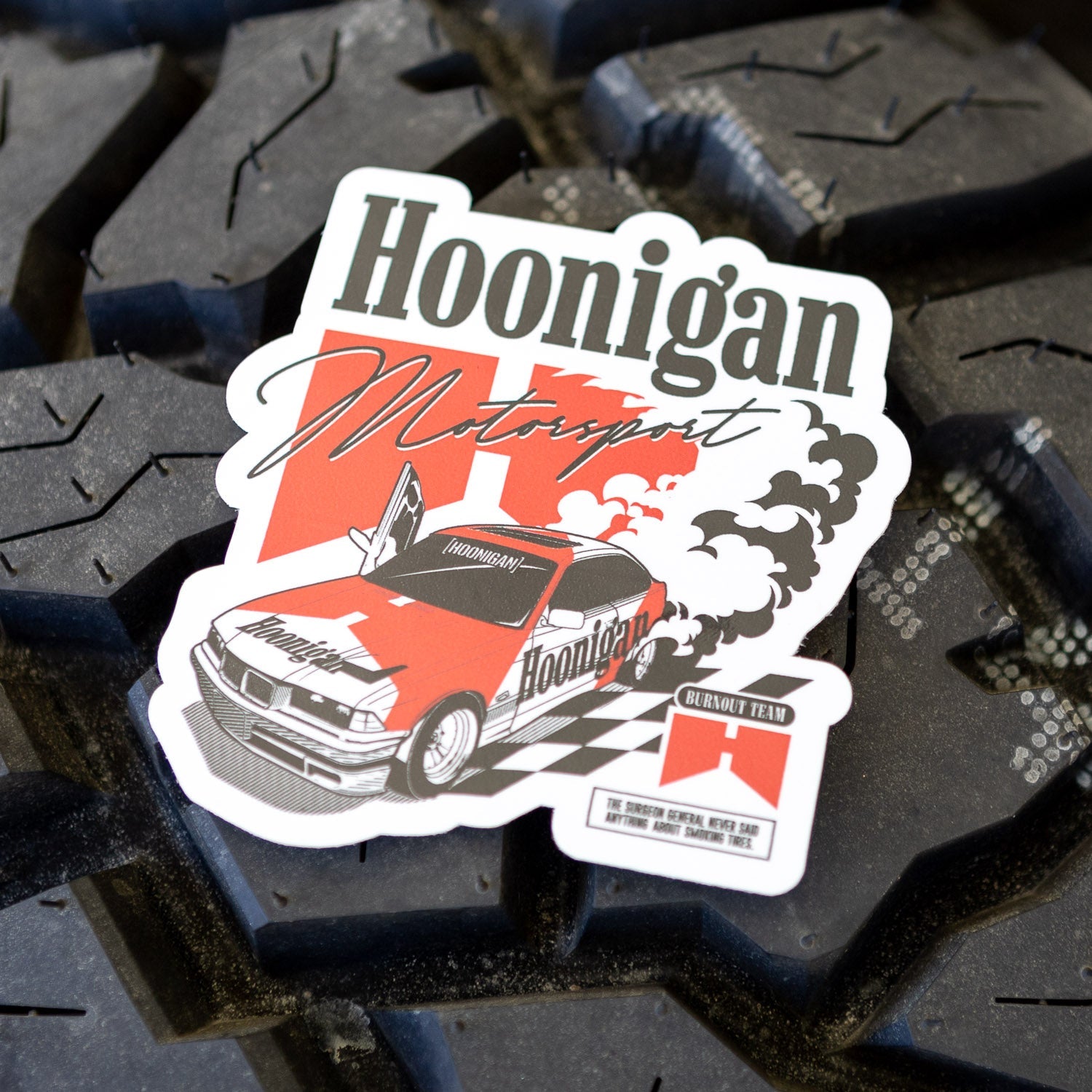 Hoonigan BURNOUT TEAM sticker featuring a classic car with smoke and checkered flag design on a tire background.