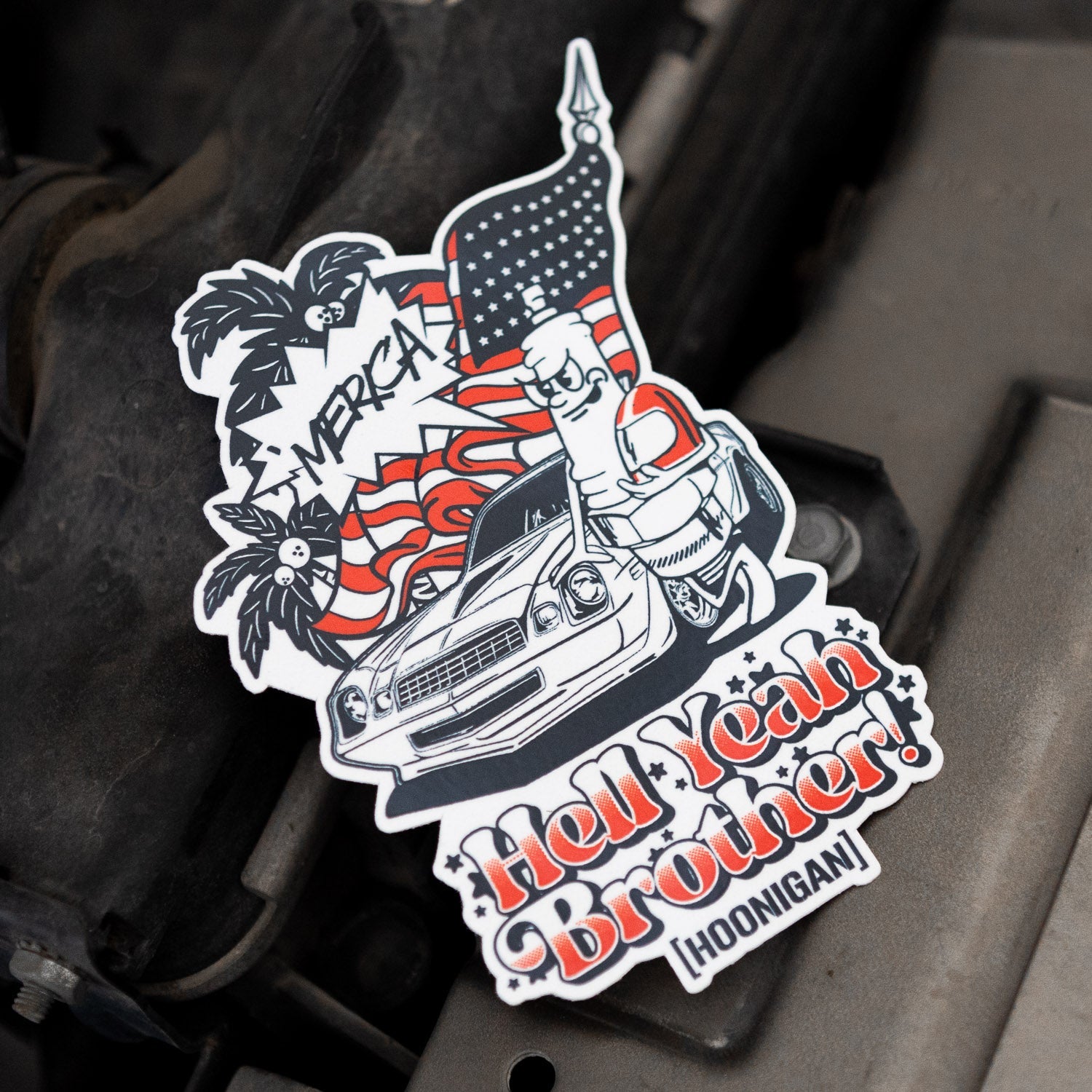 Hoonigan 'MERICA sticker featuring a classic car, palm trees, and patriotic elements, perfect for automotive enthusiasts.