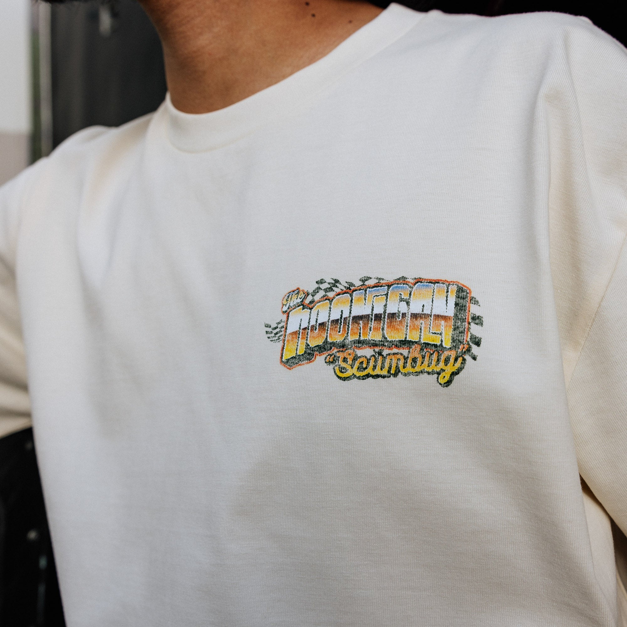 Close-up of a person wearing a Hoonigan SCUMBUG short sleeve t-shirt featuring a colorful logo on the chest.
