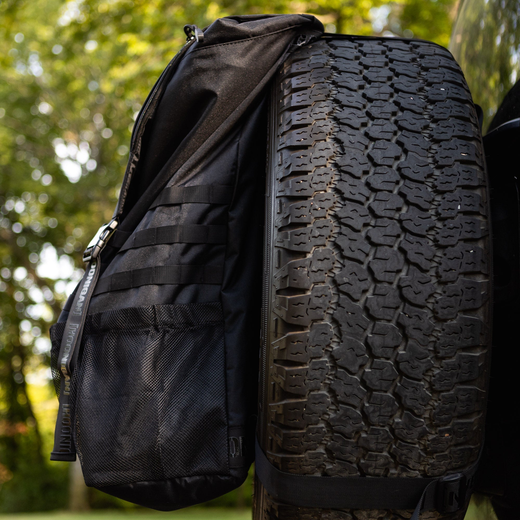 Hoonigan CENSOR BAR backpack attached to a spare tire, featuring a sleek design and multiple storage compartments.